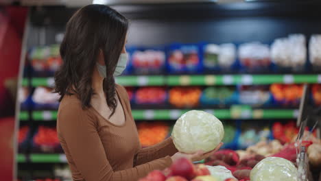 A-woman-in-a-mask-in-a-supermarket-chooses-fruits-and-vegetables-holding-cabbage-in-her-hands-in-a-store